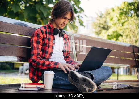 Der Laptop liegt auf den Beinen. Der Student ist im öffentlichen Park draußen. Stockfoto