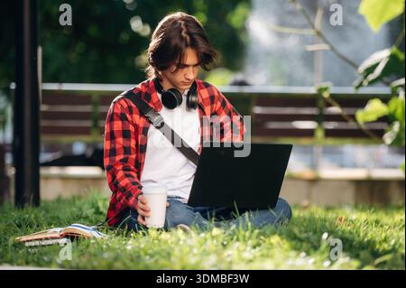 Der Laptop liegt auf den Beinen. Der Student ist im öffentlichen Park draußen. Stockfoto