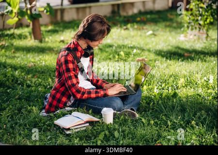 Der Laptop liegt auf den Beinen. Der Student ist im öffentlichen Park draußen. Stockfoto