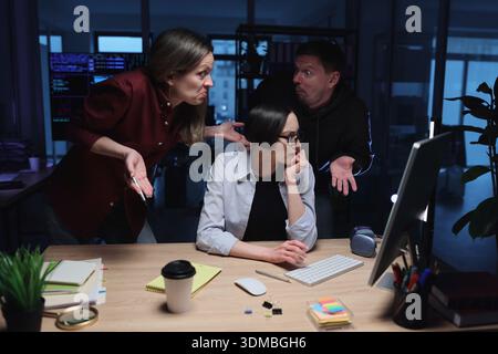 Drei Kollegen führen eine lebhafte Diskussion, während sie spät in einem modernen Büro während der Abendstunden arbeiten Stockfoto