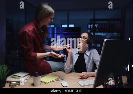 Zwei Kollegen teilen einen freudigen Moment, während sie spät in einem modernen Büro arbeiten, das voller Technologie und Kreativität ist Stockfoto