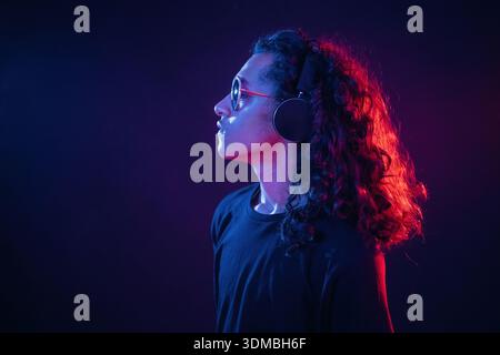 Langes Haar, Kopfhörer, Seitenansicht. Der Kerl ist nachts drinnen mit Neonlicht. Stockfoto