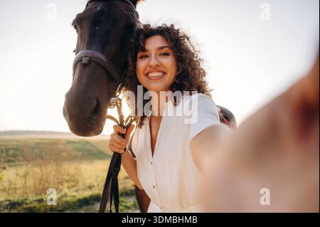Selfie machen. Frau in weißem Kleid ist mit Pferd auf dem Feld. Stockfoto