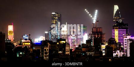 Skyline der Nachtstadt mit beleuchteten Hochhäusern, farbenfrohen Neonlichtern und einem Baukran, der eine V-Form im Vordergrund unter einem Hektar bildet Stockfoto