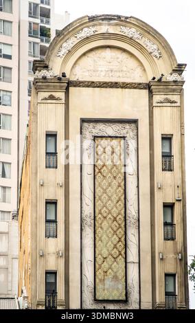 Vorderansicht der verzierten historischen Gebäudefassade mit gewölbtem Giebel, geschnitzten Steindetails und hoher dekorativer Platte, flankiert von einem modernen Hochhaus Stockfoto