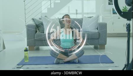 Sitzende Koreanerin in Workout-Kleidung, die Yoga auf blauer Matte zu Hause demonstriert, mit Ringlicht-HUD Stockfoto