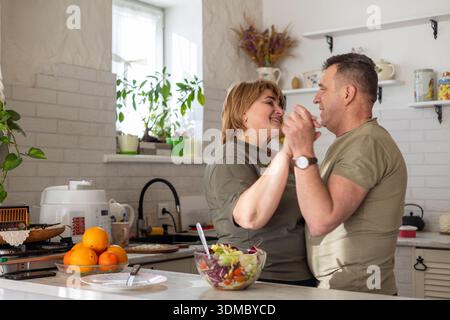 Ein reifes Paar teilt einen sanften, romantischen Tanz in ihrer Küche, während es zusammen Essen zubereitet. Ein warmer Tag der Liebe, der Verbindung, der Familie Stockfoto
