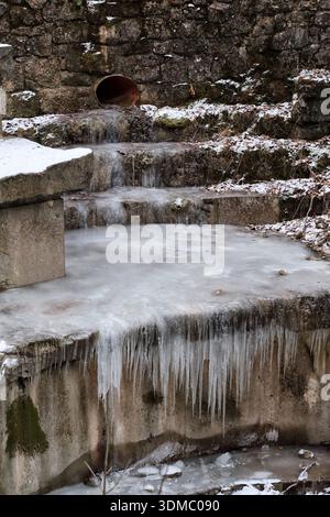 Gefrorener Bach mit Eiszapfen in rauem Gestein Stockfoto