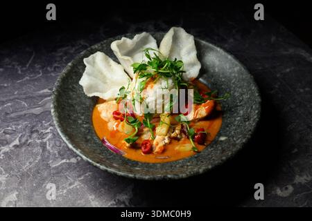 Ein Teller mit viel roter Sauce und Reis. Der Teller steht auf einem dunklen Tisch Stockfoto