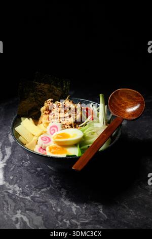 Traditionelle japanische Ramen-Schüssel mit gehacktem Hühnchen, weich gekochtem Ei, frischem Gemüse und Algen, präsentiert auf einem dunklen Holztisch zum Restau Stockfoto