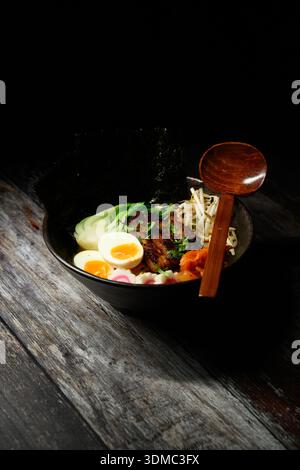 Eine Schüssel Essen mit einem Löffel darin. Die Schüssel ist schwarz und der Löffel aus Holz Stockfoto