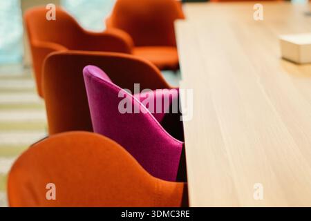 Moderne Inneneinrichtung des Konferenzraums mit Sitzgelegenheiten. Moderner Tagungsraum mit farbenfrohen Polsterstühlen neben langen Holztas Stockfoto