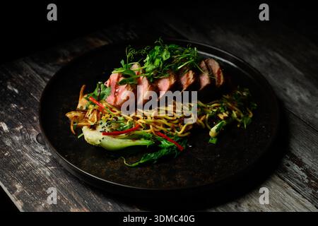 Eine Platte mit Fleisch und Gemüse mit einer schwarzen Platte. Der Teller ist voller Essen und sieht köstlich aus Stockfoto