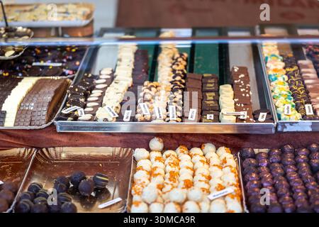 Auswahl an handgefertigten Pralinen, Pralinen und Trüffeln, die auf Tabletts an einem Marktstand ausgestellt werden, mit handgemachten Aromen, Toppings und reichhaltigen, verlockenden Aromen Stockfoto