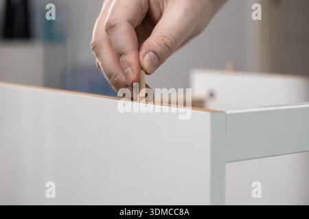 Nahaufnahme einer Einzelperson, die sorgfältig einen Holzdübel in eine weiße Spanplatte legt, symbolisiert Möbelbau, persönliches Handwerk Stockfoto