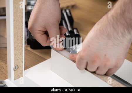 Nahaufnahme der Hände einer Person, die Elemente neuer weißer Möbel miteinander verbinden, was den Prozess der Inneneinrichtung und der Modernisierung der Inneneinrichtung darstellt Stockfoto