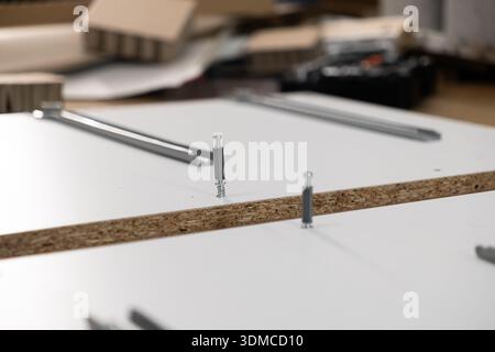 Draufsicht der weißen Spanplattenplatte mit teilweise eingelegten Nockenverriegelungsbeschlägen und sichtbaren Schrauben, Abbildung der Flatpack-Möbelbaugruppe, DIY-Konfiguration Stockfoto