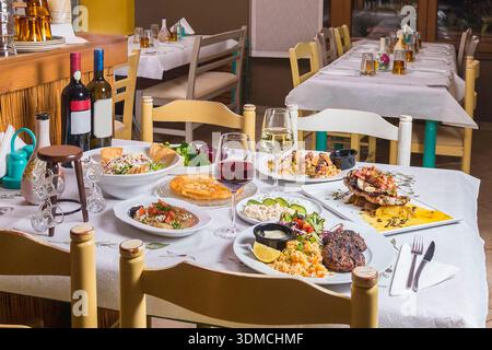 Authentische griechische und mediterrane Gerichte, einschließlich gegrilltem Fleisch, Meeresfrüchten und Salaten, auf einem wunderschön gedeckten Tisch in zwangloser Taverne-Atmosphäre, gem Stockfoto