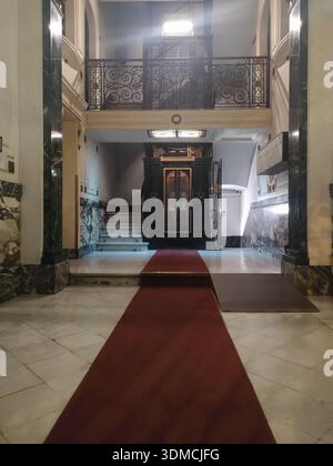 Detail einer alten Lobby eines Wohngebäudes im oberen Bereich von ​​Barcelona, Teppich von ​​red, Marmordekoration und Käfigaufzug Stockfoto