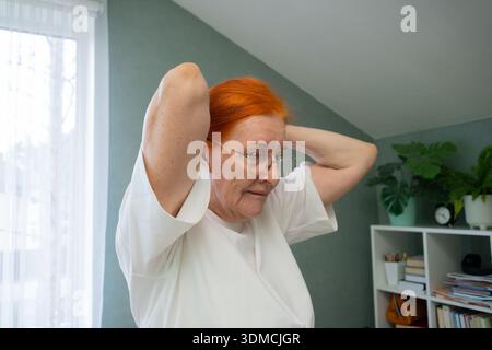 Eine siebzig-jährige Frau steht bei einer sanften Aufwärmübung mit hoch erhobenen Armen. Aktivität fördert Mobilität und Gesundheit im Schulterbereich Stockfoto
