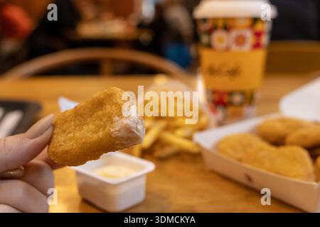 Posen, Polen - 19. November 2025: Nahaufnahme einer Hand mit einem knusprigen Hähnchennugget mit weißer Sauce, McCafe-Tasse und Pommes Stockfoto