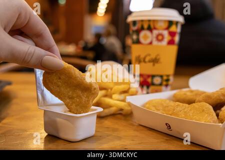 Poznan, Polen - 19. November 2025: Nahaufnahme einer Person, die einen knusprigen McDonald's Chicken Nugget in Sauce taucht, mit einer McCafe Kaffeetasse und fr Stockfoto