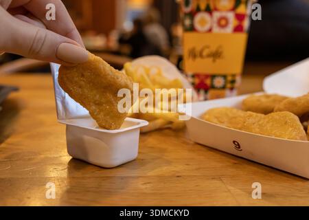 Poznan, Polen – 19. November 2025: Chicken Nugget von Hand in Soße tauchen und ein zwangloses Fast-Food-Menü mit Pommes frites und einem Markengetränk von McCafe beschreiben Stockfoto