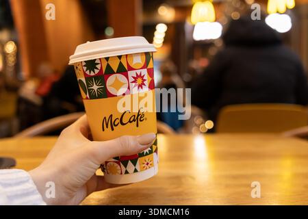 Posen, Polen - 19. November 2025: Eine Person hält eine McCafe Kaffeetasse mit farbenfrohen festlichen Mustern, die ein herrliches warmes Getränk symbolisiert Stockfoto