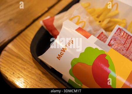 Poznan, Polen – 19. November 2025: Eine detaillierte Ansicht der McWrap Fast Food-Verpackungen, goldenen Pommes Frites und Ketchup von McDonald's, präsentiert auf einem schwarzen Tram Stockfoto