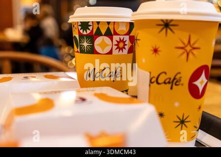 Posen, Polen - 19. November 2025: Kaffeetassen mit der Marke McCafe, die mit lebhaften Weihnachtsmustern und weißen Essensboxen verziert sind, die Convenie symbolisieren Stockfoto
