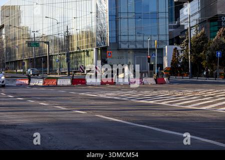 Posen, Polen - 19. November 2025: Städtische Straßenkreuzung mit temporären Barrieren und einem Fußgängerübergang, ergänzt durch ein modernes Glasbüro b Stockfoto