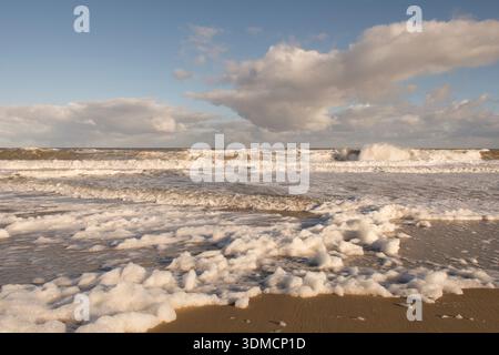 Weißer Meeresschaum von einem stürmischen Meer, das am Strand in Walcott, Norfolk, Großbritannien, unter blauem Himmel auftaucht, jetzt ist der Sturm vorüber, Dezember Stockfoto