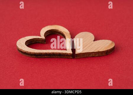 Zwei hölzerne Herzhälften, die durch einen leuchtenden roten Hintergrund getrennt sind, mit komplizierten lasergeschnittenen Details und sanfter Beleuchtung. Stockfoto