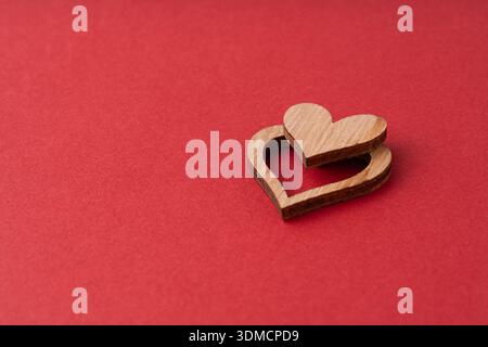 Eine minimalistische Komposition mit zwei Holzherzen mit warmer Textur auf einem leuchtend roten Hintergrund, die Gefühle von Liebe, Wärme und handgefertigtem Qua weckt Stockfoto
