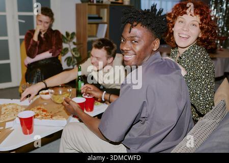 Gruppe junger Erwachsener Freunde, die sich treffen und Pizza zu Hause essen Stockfoto