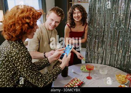 Junger kaukasischer Mann und zwei junge kaukasische Frauen machen Fotos auf der Party Stockfoto