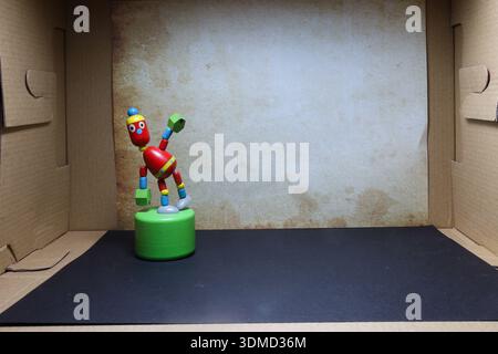 Farbenfrohe Holzfigur in einer Pappanlage, die humorvoll die Grenzen unseres Raumes und unserer Fantasie repräsentiert Stockfoto