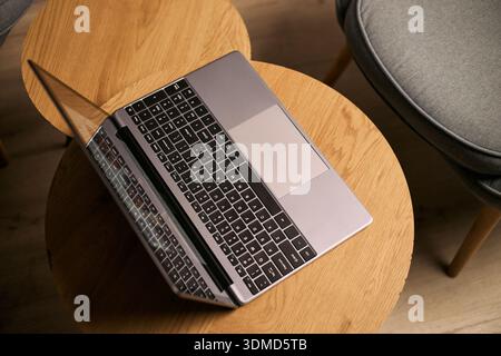Laptop auf rundem Holztisch im modernen Innenraum, Gerät für Online-Unterricht oder Fernunterricht positioniert, leerer Stuhl neben dem Arbeitsbereich sichtbar Stockfoto