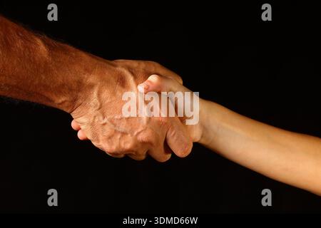 Handschlag zwischen zwei Händen vor dunklem Hintergrund – Nahaufnahme Kontrast aus Form, Textur, Verbindung und gegenseitiger Vereinbarung durch ein Unternehmen in Stockfoto