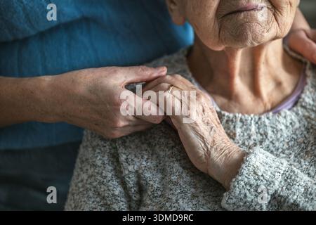 Ältere Frau, die Hände mit ihrer Betreuerin in einem Pflegeheim hält, Nahaufnahme Stockfoto
