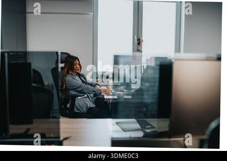 Professionelle Frau an einem Schreibtisch in einem modernen Büro mit Schwerpunkt auf Arbeitsaufgaben und Notizen Stockfoto