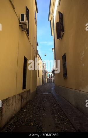 Gepflasterte und enge Gasse mit klarem Himmel darüber, in einer italienischen Stadt Stockfoto
