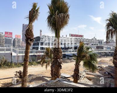 Blick auf den Fluss entlang der Nil Corniche in Kairo, Ägypten, mit Palmen, städtischer Infrastruktur am Wasser und einem schwimmenden Restaurant am Nil R Stockfoto