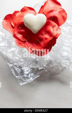 Ein helles, cremefarbenes Herz auf roten künstlichen Blättern, fixiert mit Herznadeln in Form eines Herzens für Heimwerker, Hobby, Kunsthandwerk, Muttertag, Valentinstag, Stockfoto