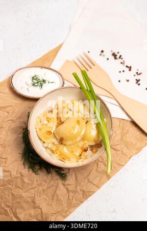 Hausgemachter Varenyky mit Kartoffelfüllung, gebratenen Zwiebeln und frischem Dill, serviert mit Holzgabel auf Pergamentpapier. Rustikale und gemütliche Essensszene. Stockfoto