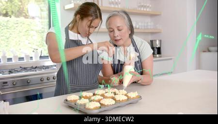 Mutter und Tochter in Nadelstreifenschürzen, die Cupcakes in der Küche mit Paspelbeutel und Streuselglas zubereiten Stockfoto