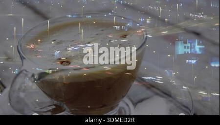 Glasbecher mit Griff, der den aufschäumenden Kaffee auf einer Untertasse im Café hält, Löffel, Stadtlichter Stockfoto