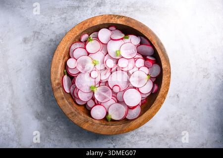 Rettichscheiben in Holzschale auf einer hellen Betonoberfläche angeordnet. Frische Bio-Produkte für gesunde Ernährung und minimalistisches Design Stockfoto