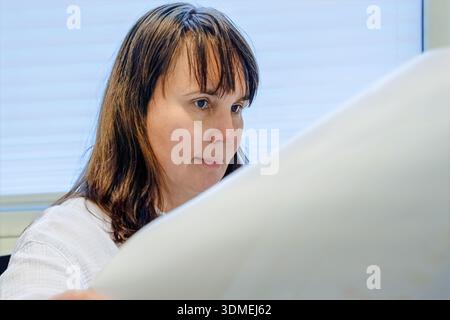 Konzentrieren Sie sich auf große Dokumente im Büro, neutrales Tageslicht durch Jalousien, weißes Hemd und ruhigen Ausdruck, qui Stockfoto
