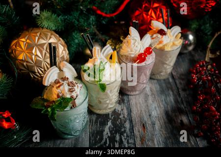 Eine Reihe von vier verschiedenfarbigen Getränken in hohen Gläsern. Die Getränke werden mit Schlagsahne und Obst belegt. Die Getränke sind auf einem Holztisch angeordnet Stockfoto